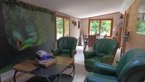 Quarto com um grande mural de uma cena florestal, poltronas de couro verde, uma mesa de centro de madeira e uma mesa de jantar com cadeiras.