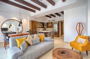 A modern living room with a sofa, coffee table, and a yellow armchair. There is a dining area with a table and chairs, and a kitchen in the background. - Awesome 2-bedroom condo with AC in vibrant Puerto Vallarta in Zona Romántica (Puerto Vallarta)
