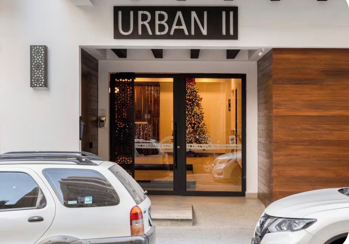 A hotel entrance with a sign reading 'URBAN II,' a Christmas tree, and a car parked in front.