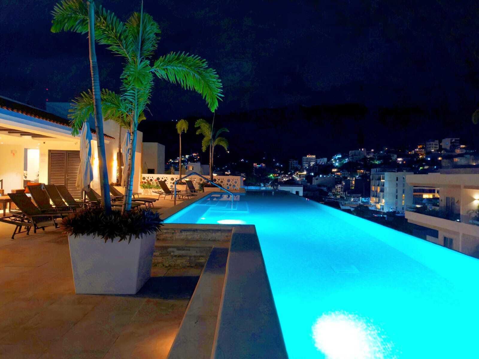 A nighttime swimming pool area with lounge chairs and palm trees.