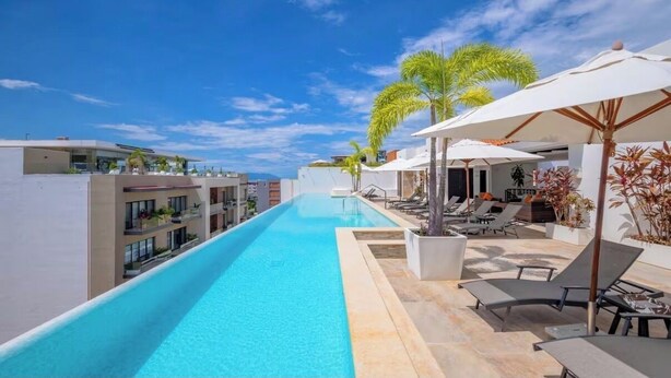 A swimming pool with lounge chairs and umbrellas, surrounded by buildings. - Awesome 2-bedroom condo with AC in vibrant Puerto Vallarta in Zona Romántica (Puerto Vallarta)