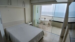 A bedroom with a bed, a small bedside table, and a wardrobe. There is a balcony with a glass door leading to an outdoor seating area. - SHB Paraíso na Praia de Pitangueiras (Guarujá)