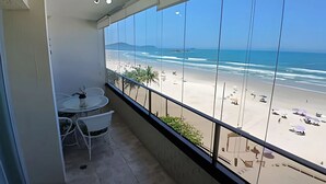 A balcony with a view of the beach, a table with chairs, and a potted plant. - SHB Paraíso na Praia de Pitangueiras (Guarujá)