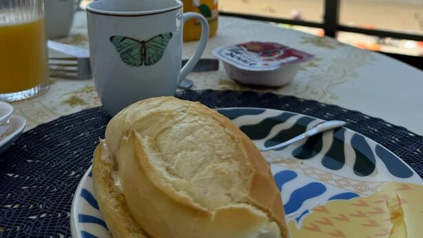 A breakfast setup with a pastry, a mug, and a juice bottle on a table with a view of the beach. - SHB Paraíso na Praia de Pitangueiras (Guarujá)