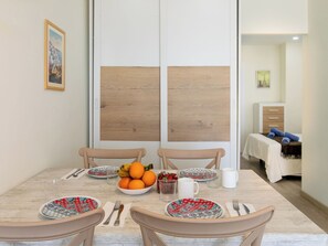A dining area with a table set for four, chairs, a bowl of fruit, and a bed in the background. - El Bungalow by Interhome (Torrox Costa)