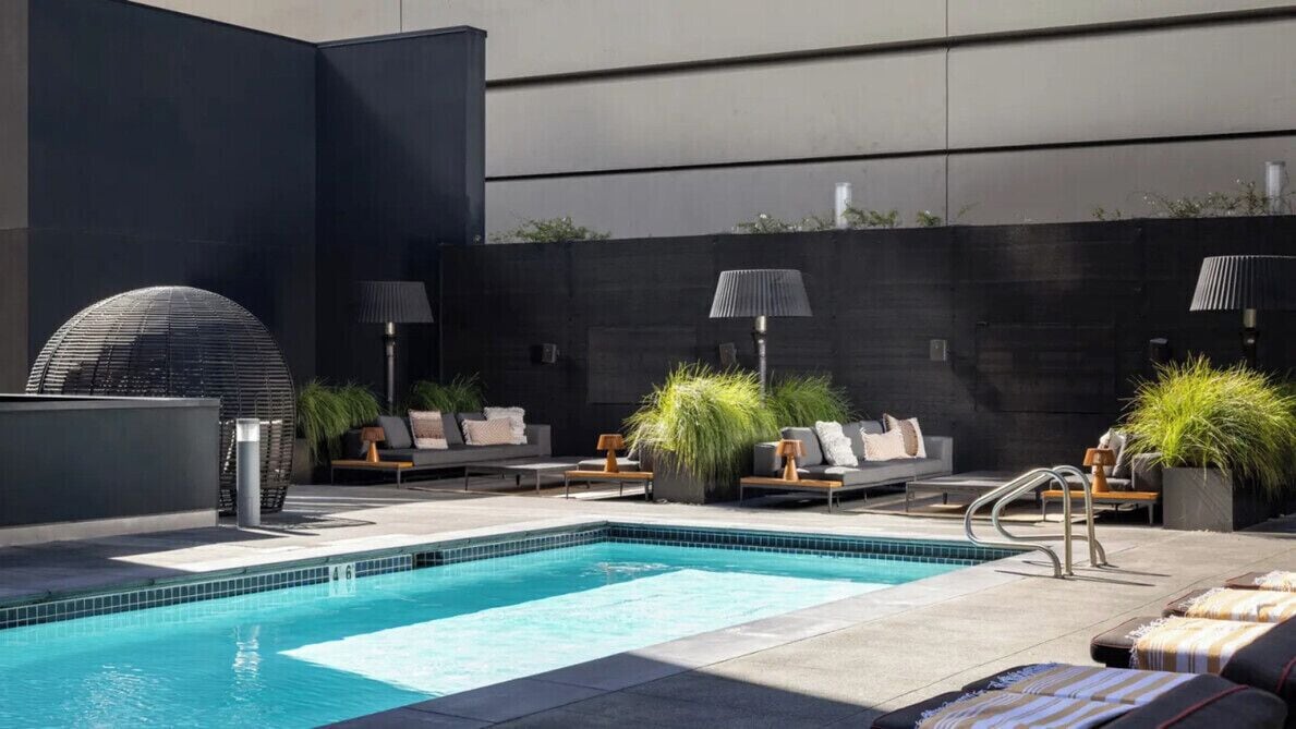 A rooftop pool area with lounge chairs, potted plants, and a modern architectural design.