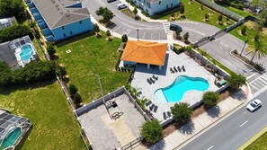 An aerial view of a residential area with a swimming pool, a curved-roofed building, and a road with vehicles. - 5BR Private Pool Home Near Disney (Kissimmee)