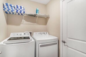 A laundry area with two washing machines, a drying rack with folded towels, and a door to the right. - 5BR Private Pool Home Near Disney (Kissimmee)