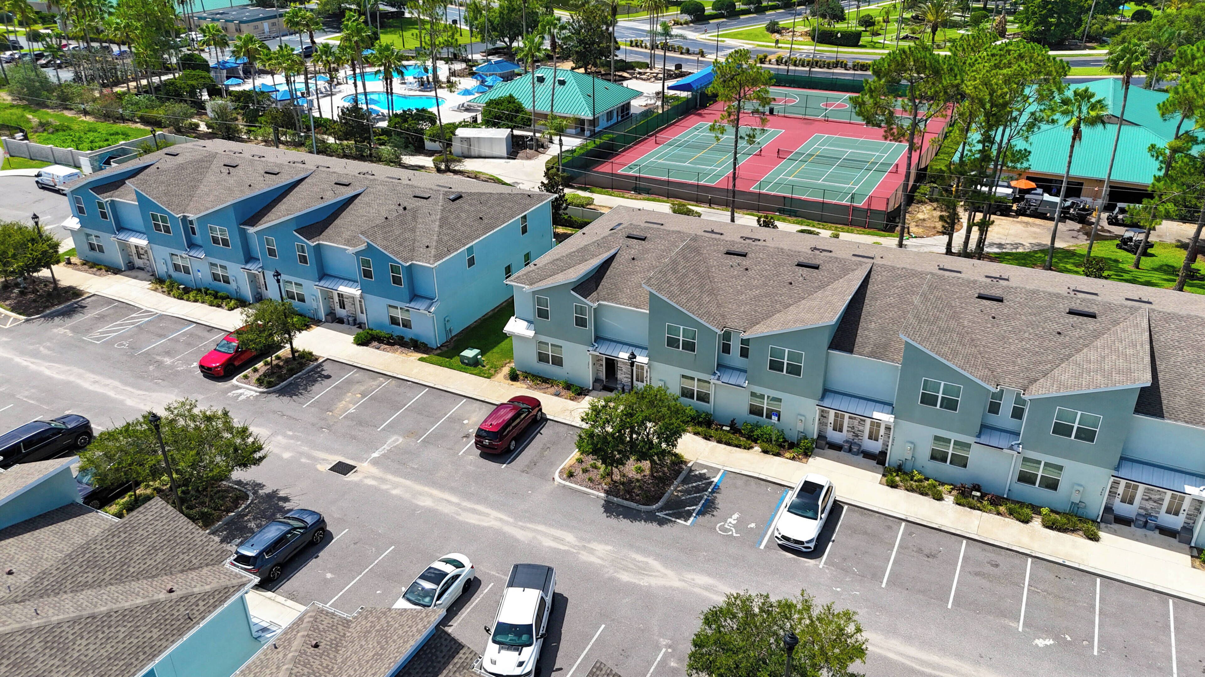 A multi-story residential building with a parking lot, adjacent to a sports complex with tennis courts.