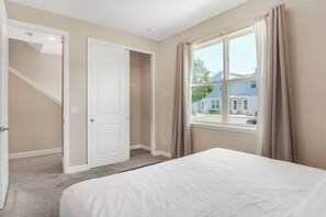 Ein Schlafzimmer mit einem Bett, einem Fenster mit Vorhängen, einer Tür und einer Treppe.
