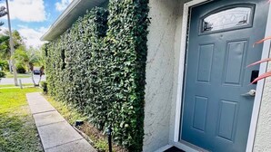 A house with a blue door, a concrete pathway, and a hedge along the side.