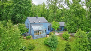 A blue house with a large glass window and a metal roof, surrounded by dense green trees. - Luxury Blue Ridge Retreat - Hot Tub - 15 Min to Early Mountain Vineyard (Stanardsville)