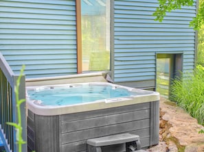 Ein Whirlpool in einem Garten mit einem gepflasterten Weg und einem Haus mit blauen Fassadenverkleidungen.