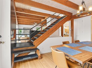 Ein modernes Interieur mit einer Holztreppe, einem Essbereich mit Tisch und Stühlen sowie Blick auf eine Küche und ein Wohnraum.