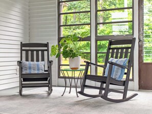 Deux fauteuils à bascule, une plante en pot et une petite table dans une pièce dotée de grandes fenêtres.