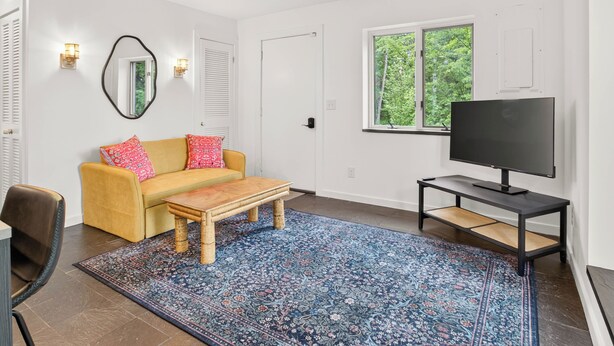A modern living room with a sofa, coffee table, TV, and a large window. - Luxury Blue Ridge Retreat - Hot Tub - 15 Min to Early Mountain Vineyard (Stanardsville)