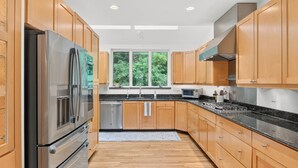 A modern kitchen with wooden cabinets, stainless steel appliances, and a window with a view of greenery. - Luxury Blue Ridge Retreat - Hot Tub - 15 Min to Early Mountain Vineyard (Stanardsville)