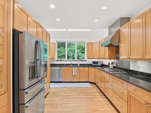 A modern kitchen with wooden cabinets, stainless steel appliances, and a window with a view of greenery. - Luxury Blue Ridge Retreat - Hot Tub - 15 Min to Early Mountain Vineyard (Stanardsville)