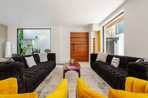A modern living room with two black sofas, a yellow armchair, and a wooden door. - Private La Roma House with Rooftop and Fire Pit (Ciudad de México)