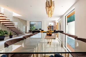 A modern living room with a glass coffee table, seating, a staircase, and a large window. - Private La Roma House with Rooftop and Fire Pit (Ciudad de México)