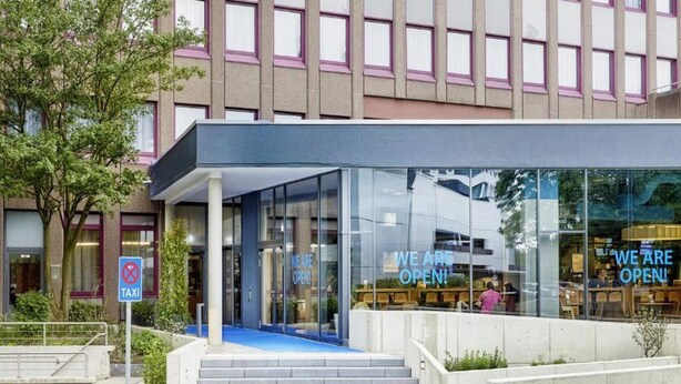 Un edificio moderno con entrada de vidrio, un letrero con la palabra 'TAXI' y un letrero que indica 'ABIERTO'.