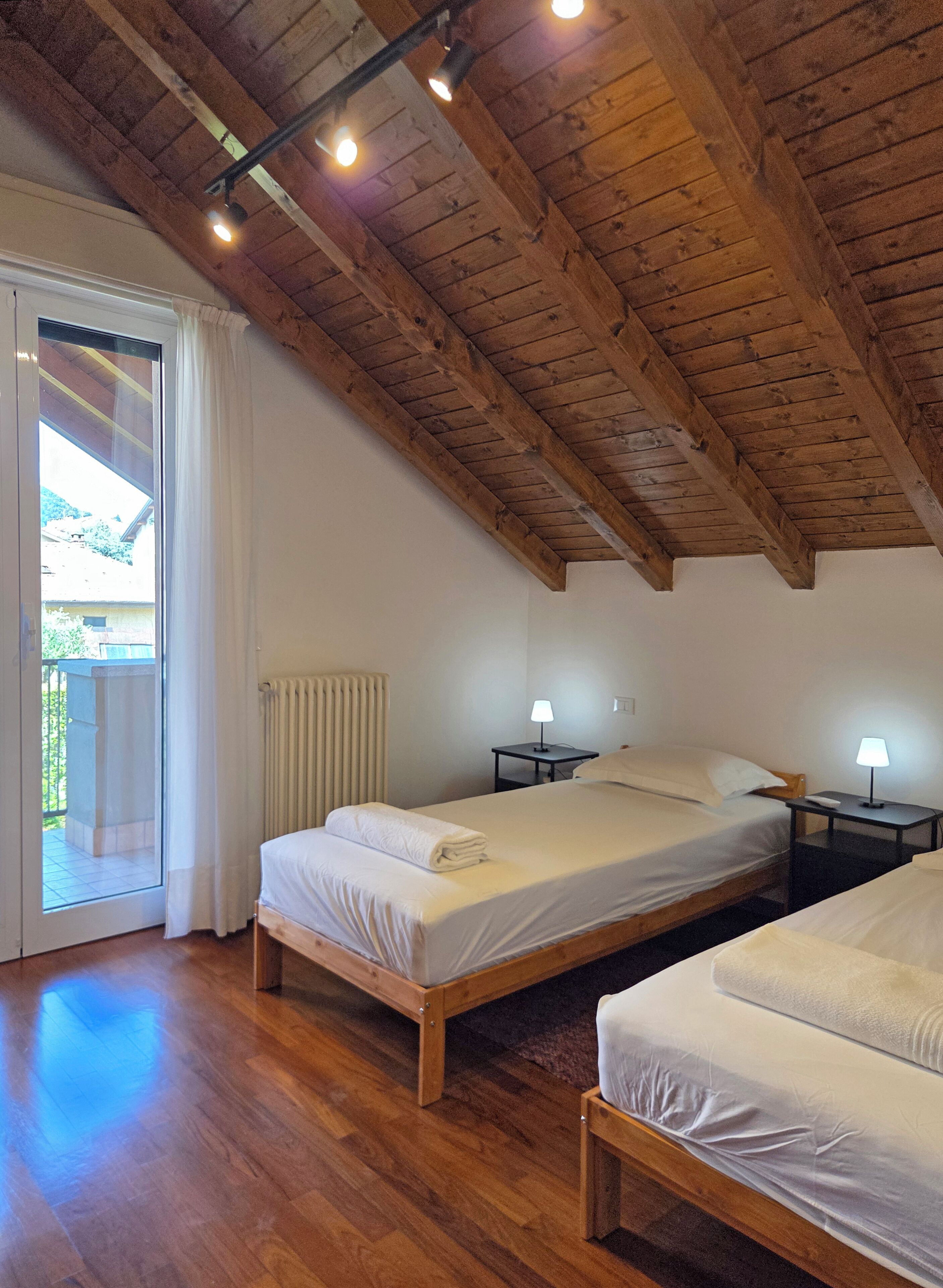 Una camera da letto con due letti, pavimento in legno, soffitto a falde e una porta scorrevole in vetro che dà su uno spazio esterno.