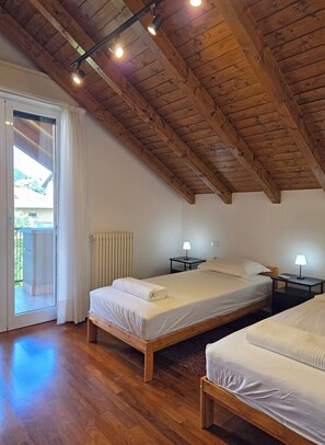 A bedroom with two beds, wooden flooring, a sloped ceiling, and a sliding glass door leading to an outdoor area. - Villa Anto • Garden Retreat Steps from Lake Como (Como)