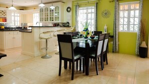 A dining area with a table set for four, a kitchen with white cabinets, and a green accent wall. - Cap Estate Private Caribbean Villa with Ocean Views (Gros Islet)