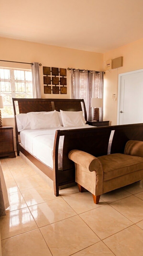 A bedroom with a bed, a sofa, a nightstand, a lamp, and a window with curtains.