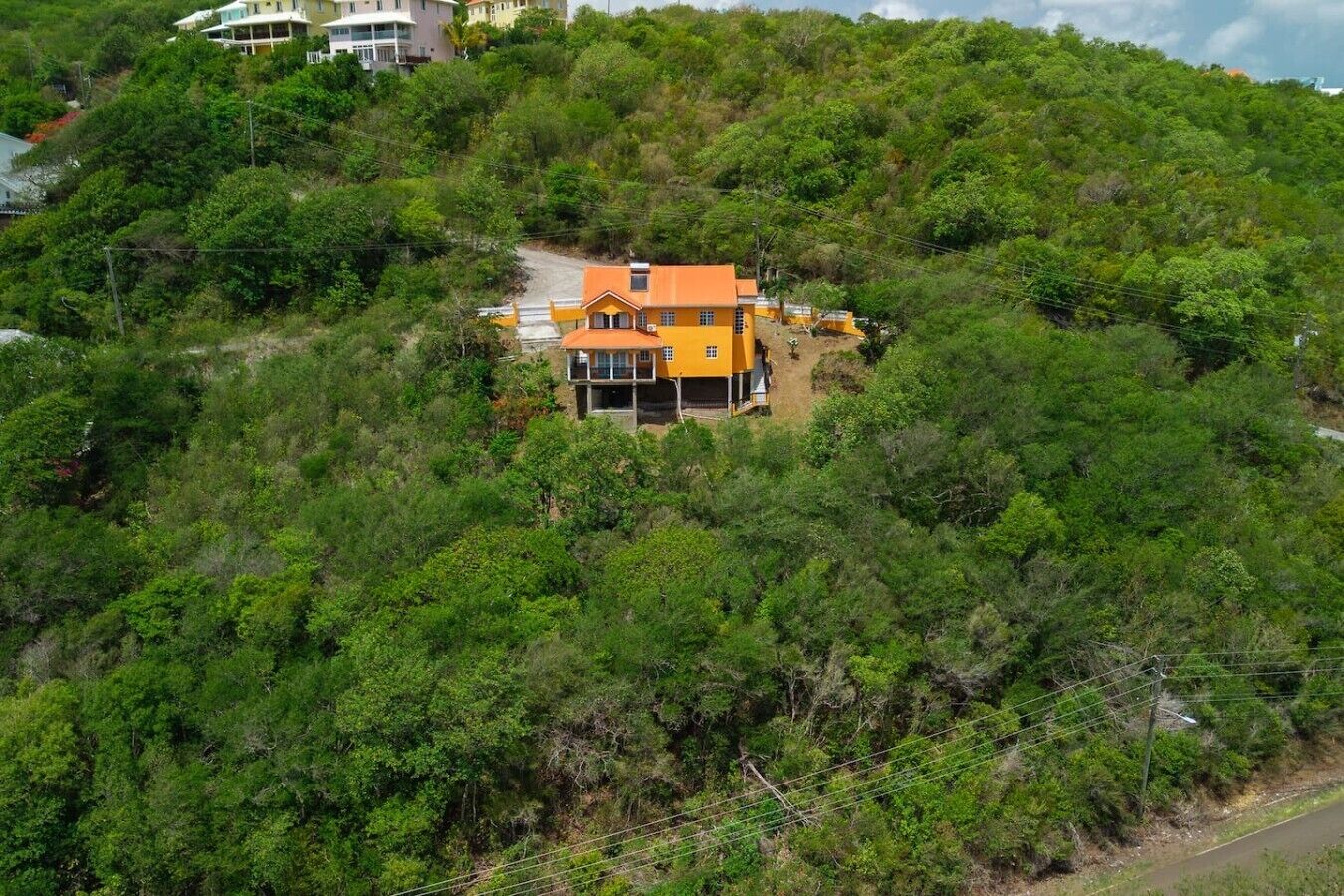 A hillside property with a single two-story building featuring a prominent orange roof and a balcony.