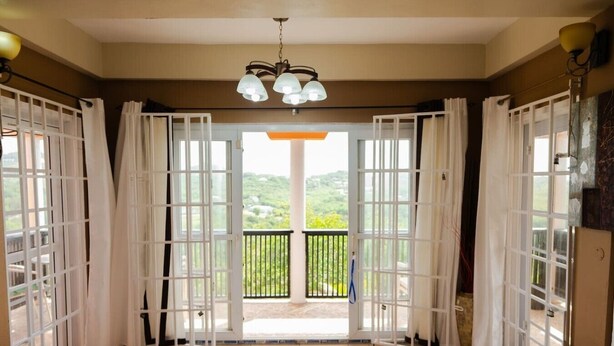 A room with a large sliding glass door leading to a balcony with a view of greenery. - Cap Estate Private Caribbean Villa with Ocean Views (Gros Islet)