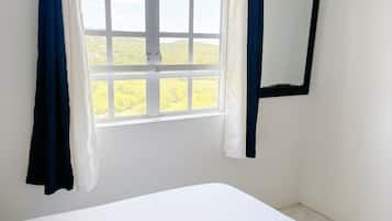 Una habitación con cama, ventana con cortinas y espejo en la pared.