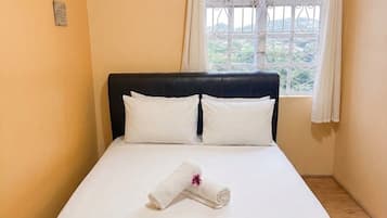 Ein Einzelbett mit schwarzem Kopfteil und weißer Bettwäsche, ein aufgerolltes Handtuch auf dem Bett und ein Fenster mit Vorhängen.