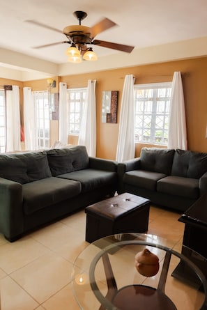 A living room with two dark sofas, a glass coffee table, and a ceiling fan.
