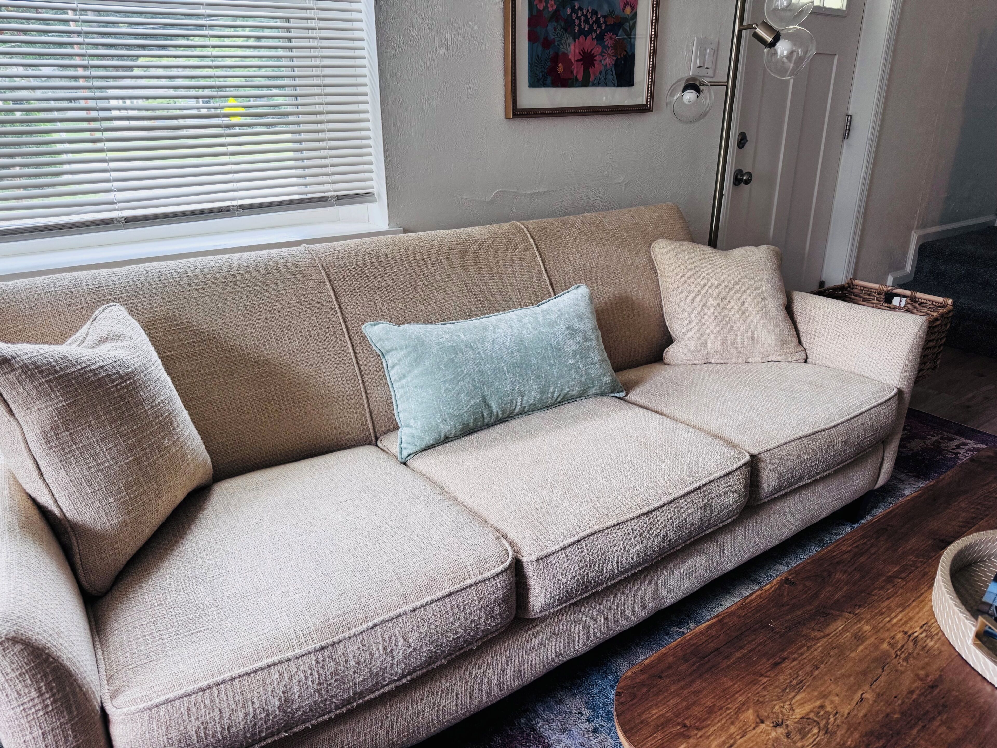 A beige sofa with two pillows, a framed floral artwork on the wall, and a wooden coffee table.