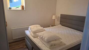 A bedroom with a bed, a bedside lamp, a window with a view, and a radiator.