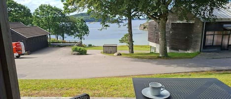 A deck with a table and chairs overlooking a body of water, a building with a sloped roof, and a parked vehicle.
