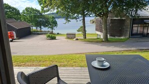 A deck with a table and chairs overlooking a body of water, a parking area, and a building with a sloped roof. - 5 Star Holiday Home in Uddevalla (Uddevalla)