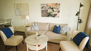 Una sala de estar con un sofá color beige, dos sillones, una mesa de centro, un mapa en la pared y una lámpara.