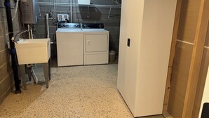 Un cuarto de lavandería con un lavamanos, dos lavadoras y un bote de basura metálico.