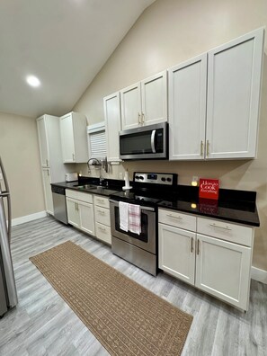 A modern kitchen with white cabinets, stainless steel appliances, and a black countertop. - Brenda Blue - Near World Cup, Stadium & Downtown (Decatur)