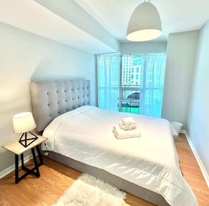 Una camera da letto con un letto grande, una lampada da comodino, vista sui palazzi attraverso una finestra e un tappeto soffice.