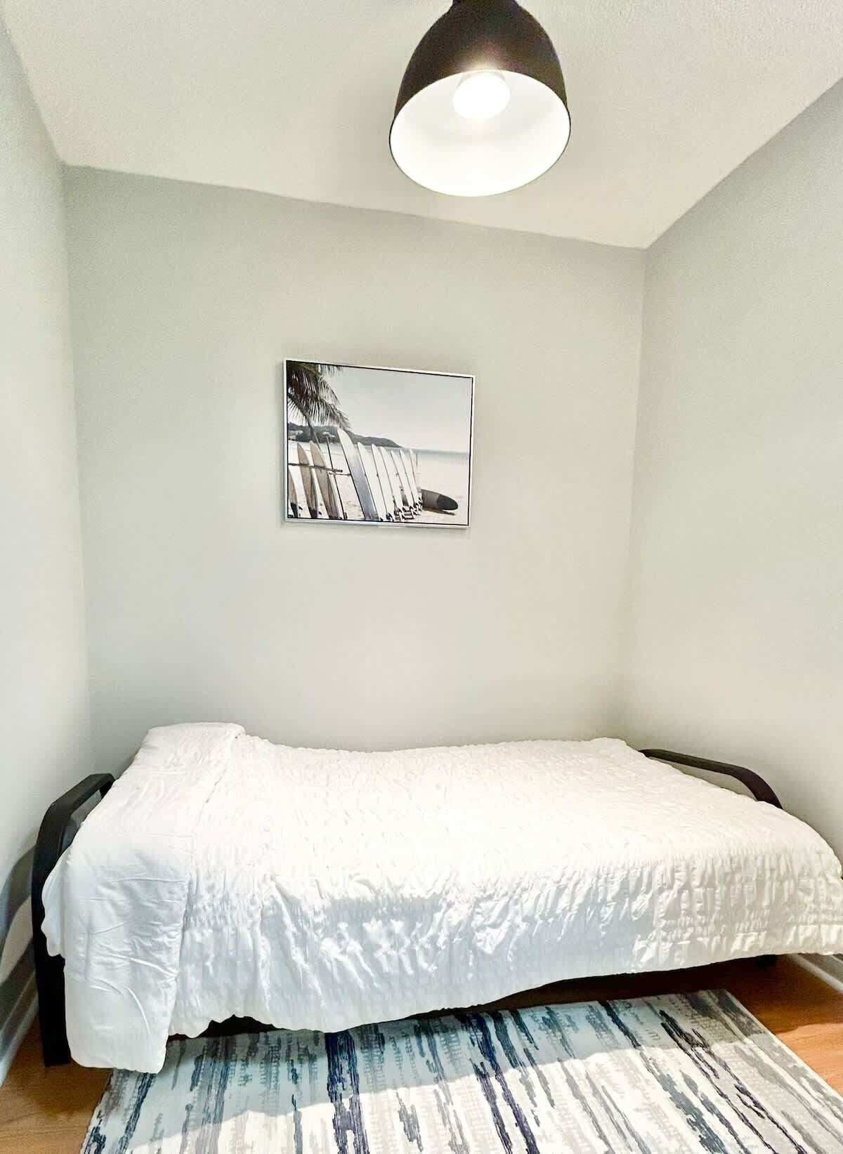 Ein Schlafzimmer mit einem Bett, einem gerahmten Bild an der Wand und einer Deckenleuchte.