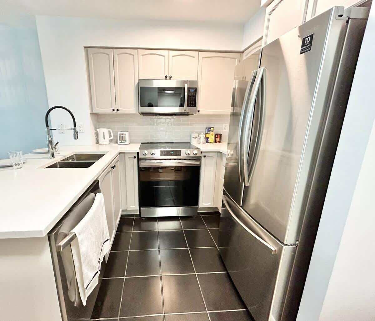 A compact kitchen with a stainless steel refrigerator, microwave, oven, and sink.