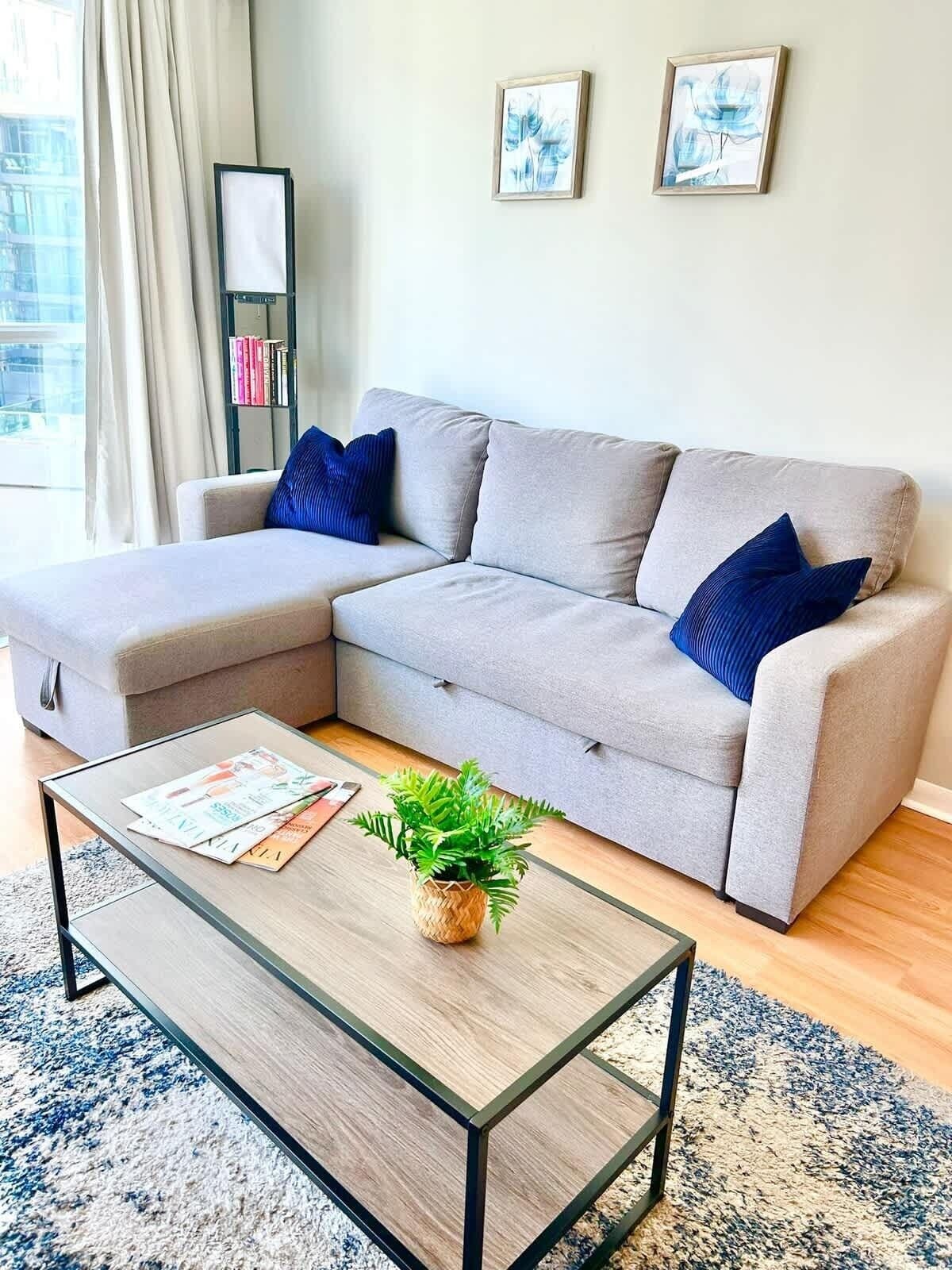 Ein modernes Wohnzimmer mit einem grauen Ecksofa, einem Glastisch und einer kleinen Pflanze.
