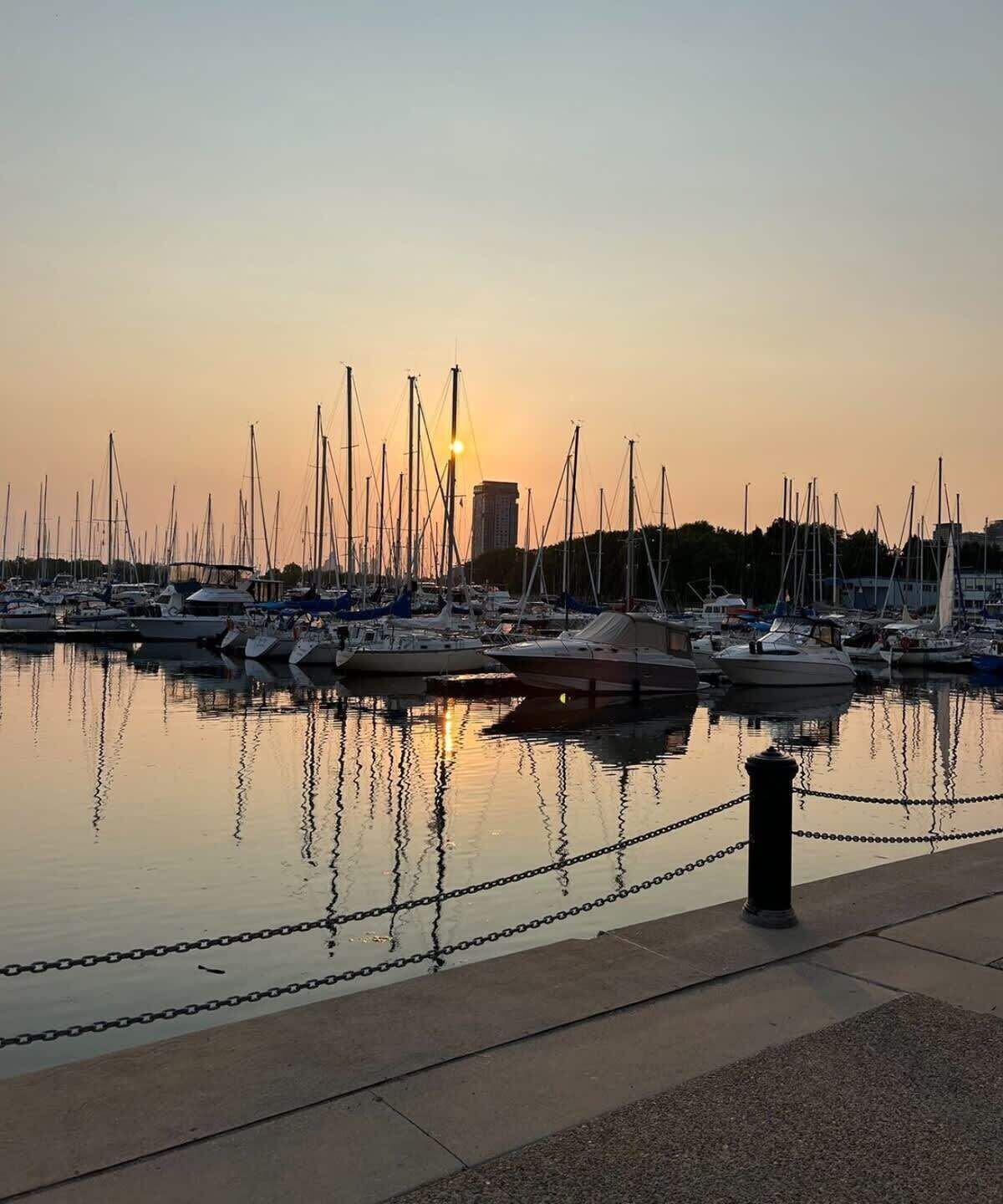 Un puerto deportivo con varias embarcaciones amarradas, cielo despejado y un atardecer.