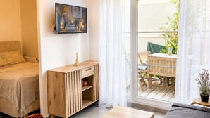 Una habitación con una cama, un armario de madera, una mesa de comedor con un expositor de vidrio para pasteles, y un balcón con mesa y sillas.