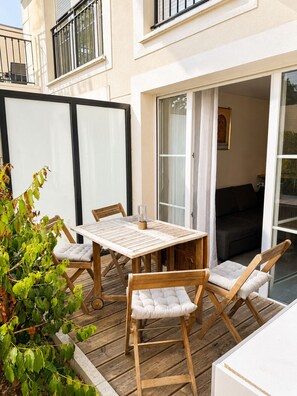 A wooden deck with a table and chairs, a sliding glass door, and a balcony with a view. - Beautiful 2-room apartment with a private garden (Le Blanc-Mesnil)