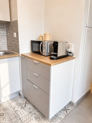 A compact kitchen with a microwave, toaster, and coffee maker on a countertop, a sink, and a cabinet with drawers. - Beautiful 2-room apartment with a private garden (Le Blanc-Mesnil)