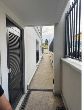 Ein schmaler Gang mit einem Metallgitter rechts, einer Tür links und einem Fenster auf der linken Seite.